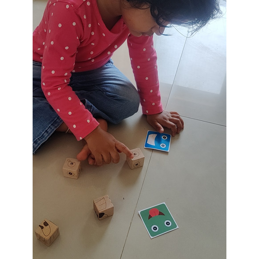 Child arranging wooden matching cubes to recreate a facial expression from a challenge card.