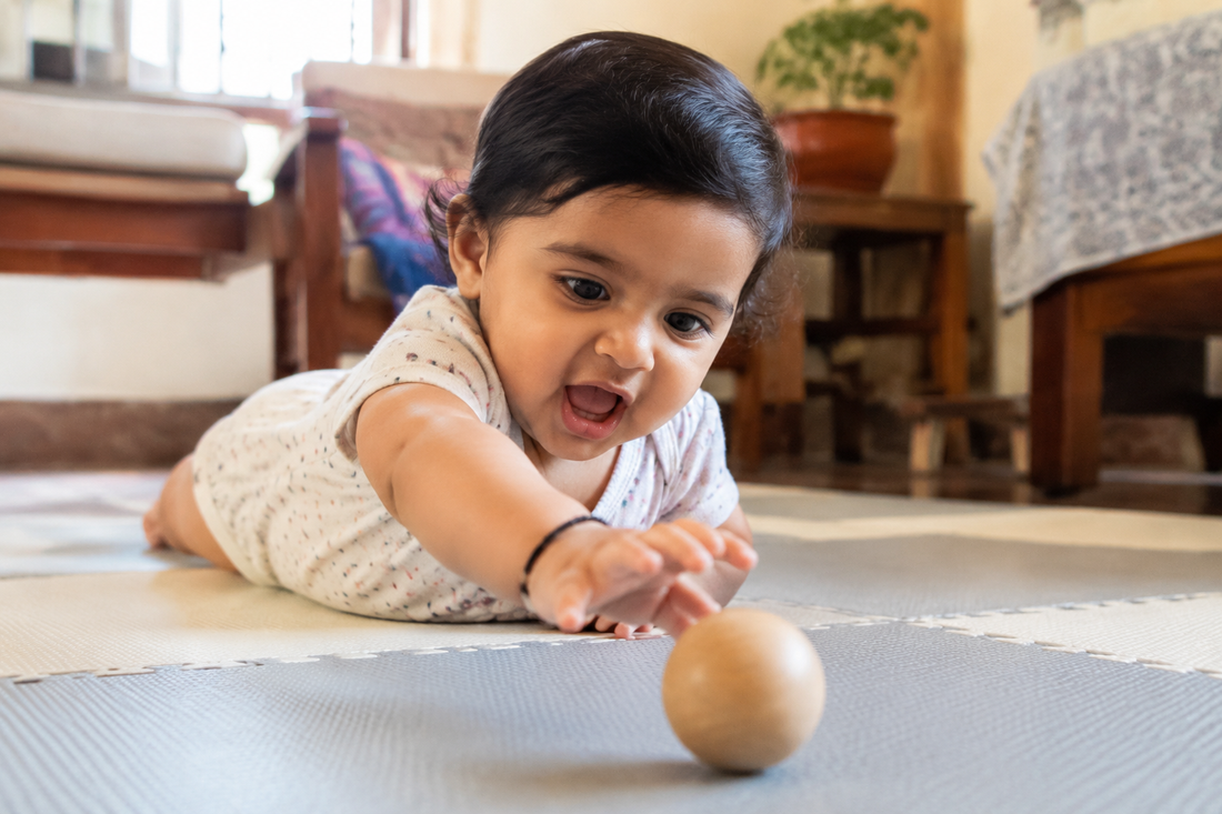 8 month old Indian baby on her forearms during tummy time, reaching forward for a wooden toy just out of reach