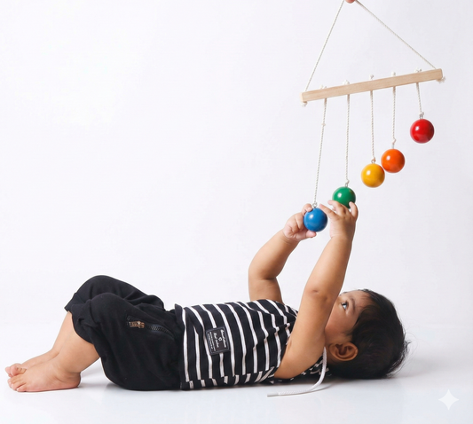 Child playing with a colorful hanging mobile toy on a white background