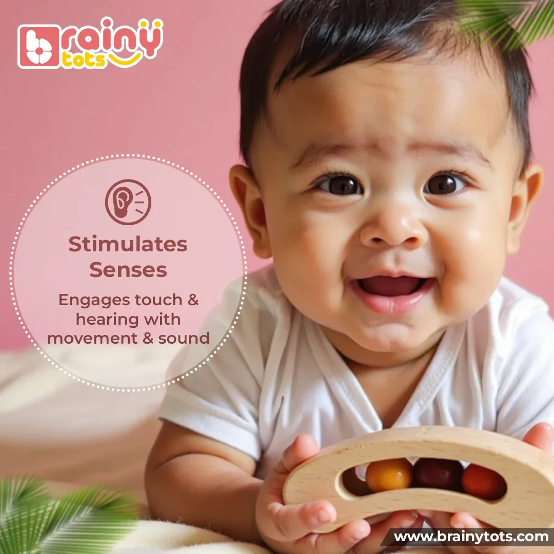 Baby holding the BrainyTots Montessori Banana Busy Beads Rattle, exploring its wooden texture and moving beads to stimulate touch and hearing through movement and sound for babies aged 2–18 months.