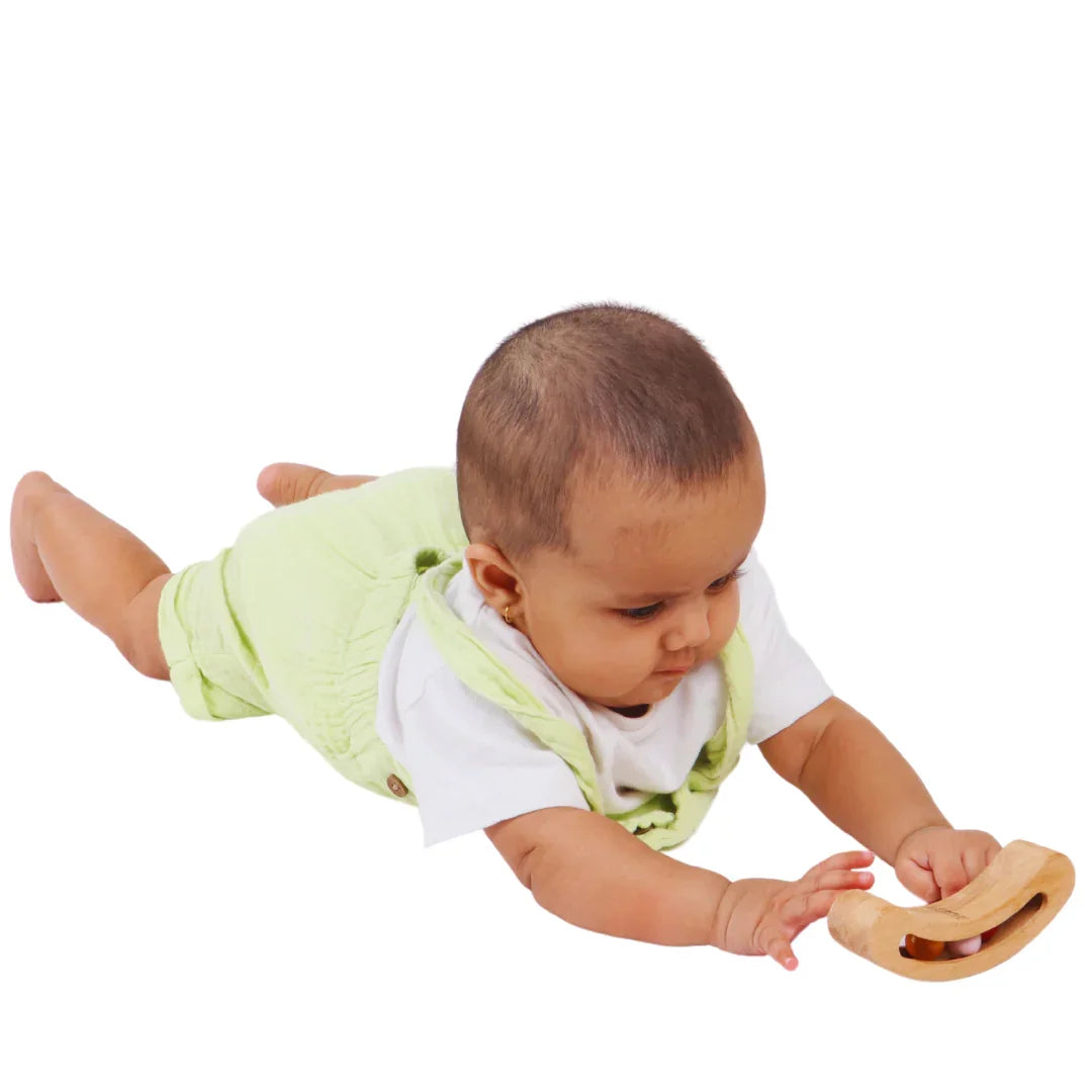 Baby reaching for the BrainyTots Montessori Banana Busy Beads Rattle during tummy time, encouraging grasping, reaching, coordination, and sensory exploration.