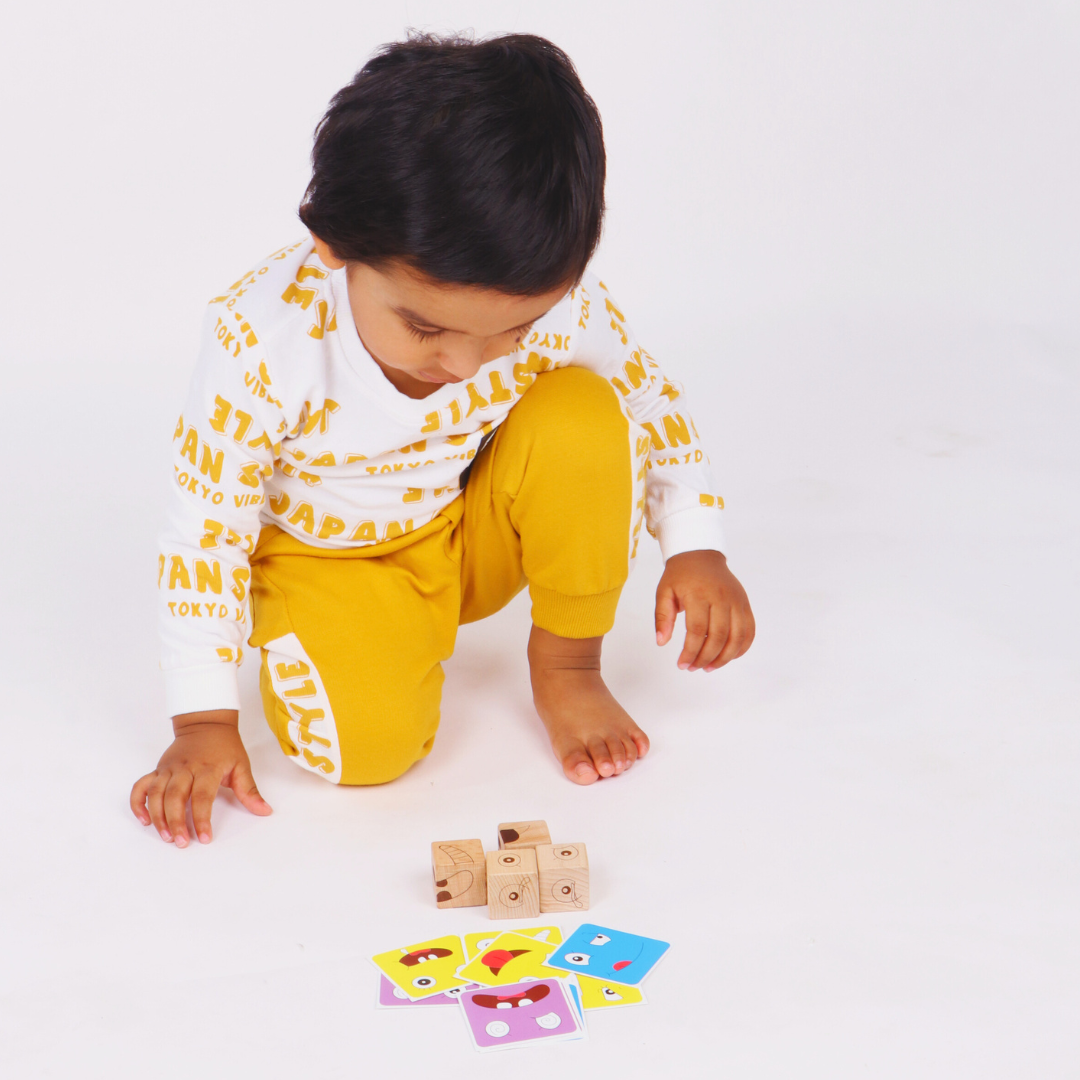 Young toddler arranging wooden emotion cubes while exploring colorful facial expression challenge cards.