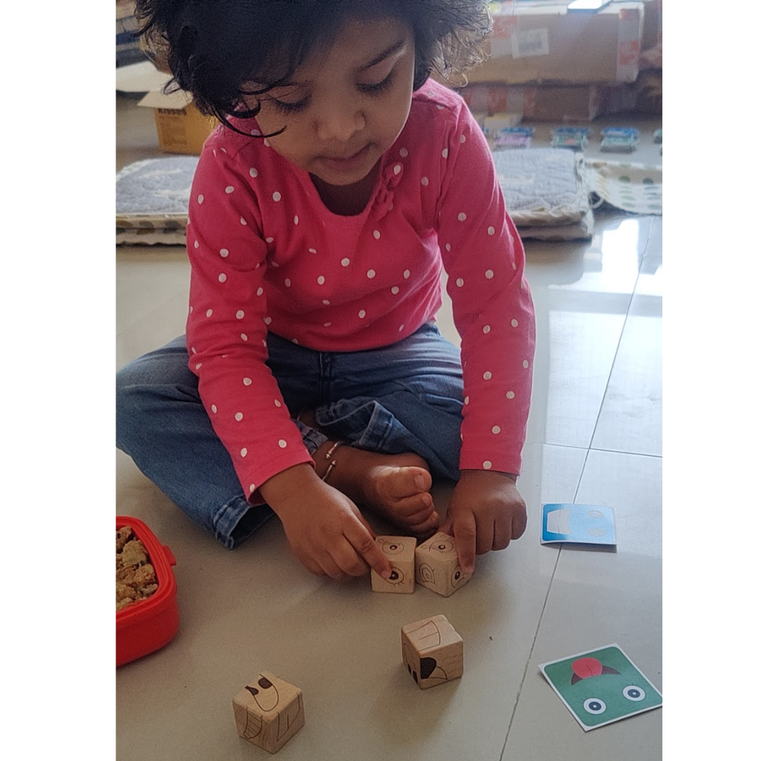 Child arranging emotion cubes to match the facial features shown on a colorful expression card.