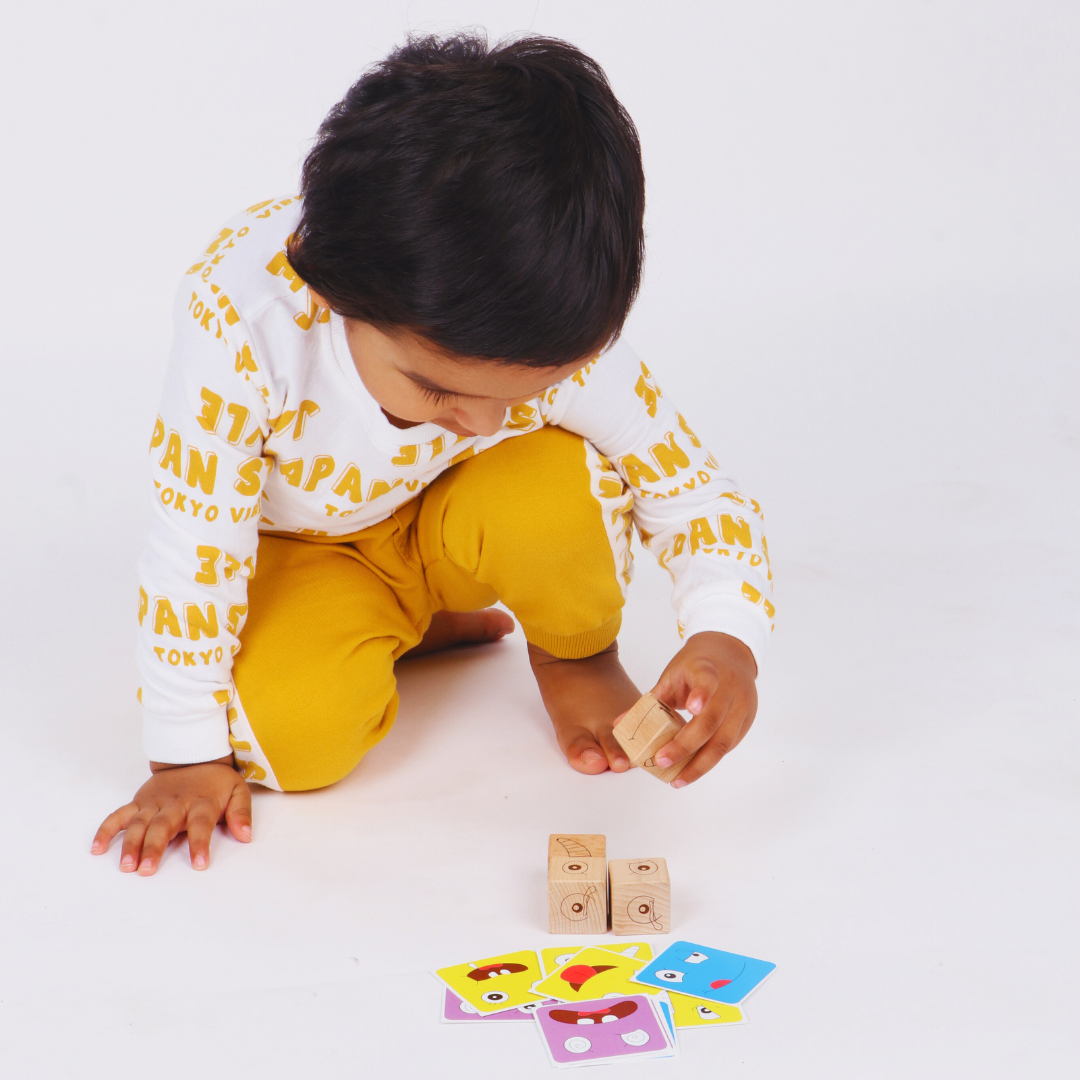 Young boy exploring wooden expression cubes and facial expression cards during a matching game.