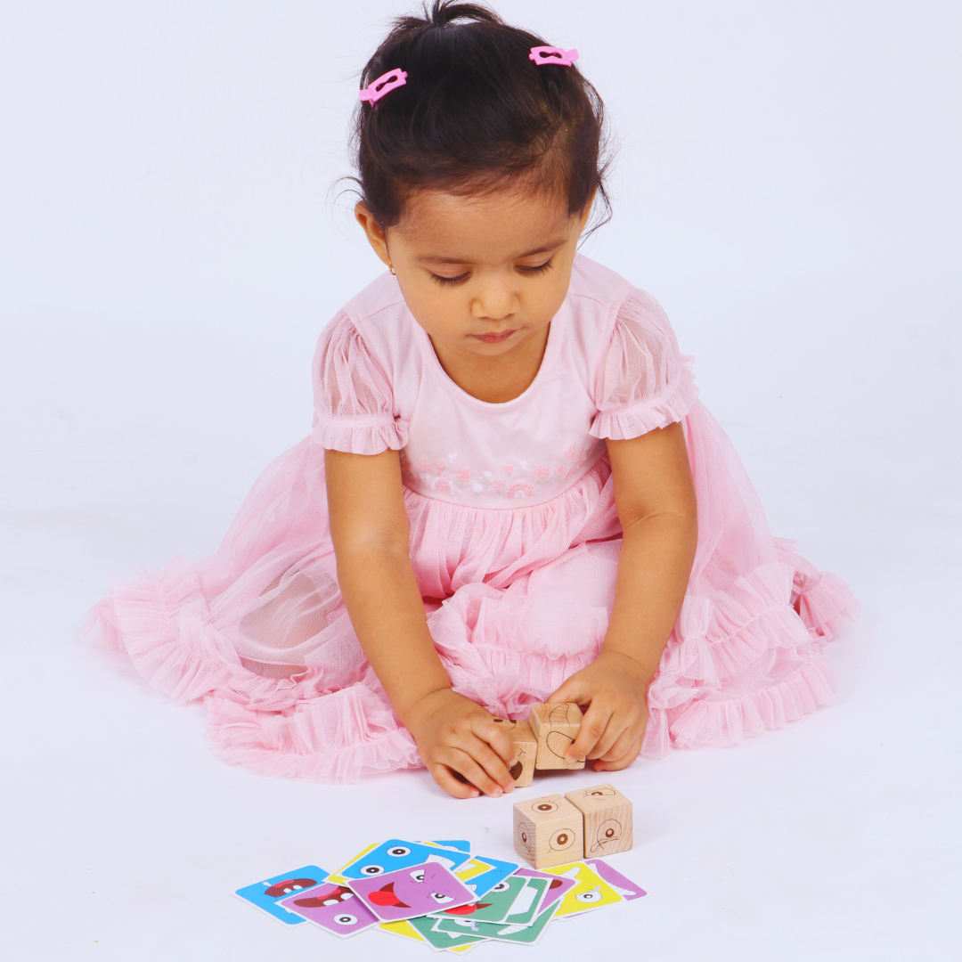 Young girl playing with BrainyTots Face Match Fun Cubes and matching facial expression cards.