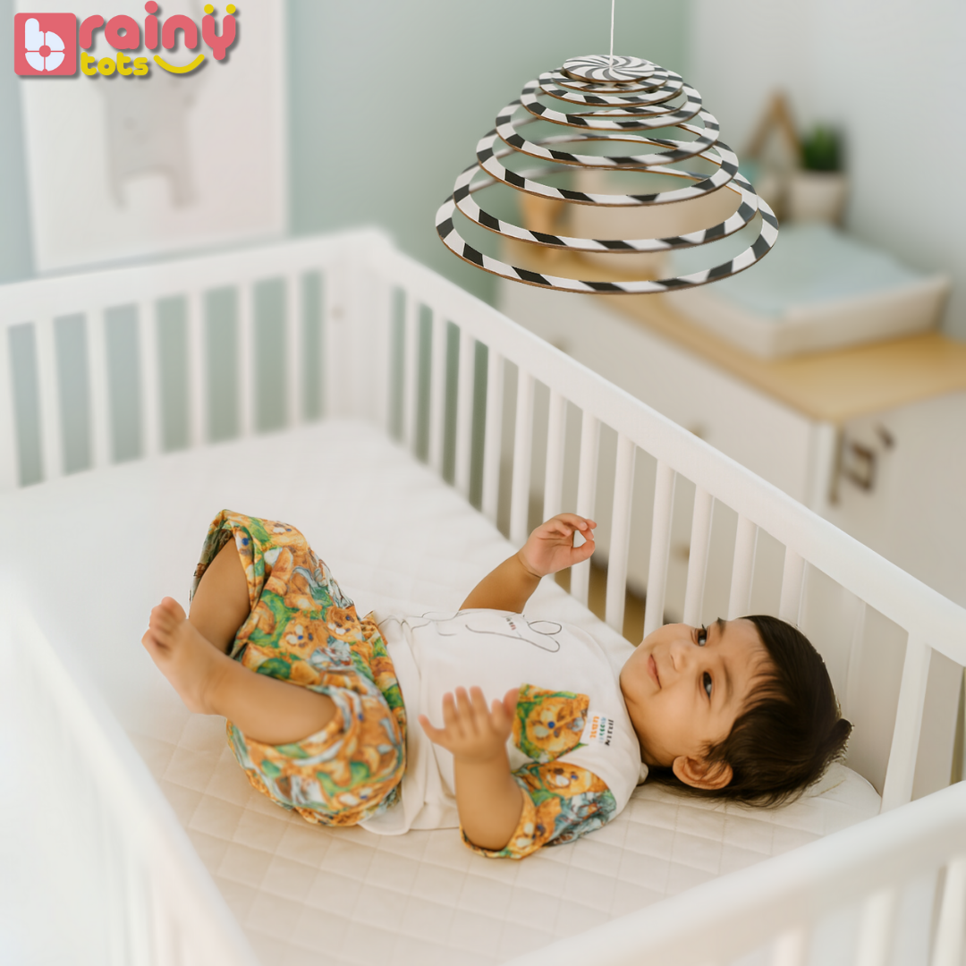 Baby lying calmly in a crib while watching the BrainyTots Dual-Sided Spiral Hanging Mobile with its high-contrast black-and-white design. This Montessori-inspired natural wooden baby mobile supports newborn visual tracking, focus, concentration, and early visual development while creating a soothing crib environment for babies aged 0–3 months.