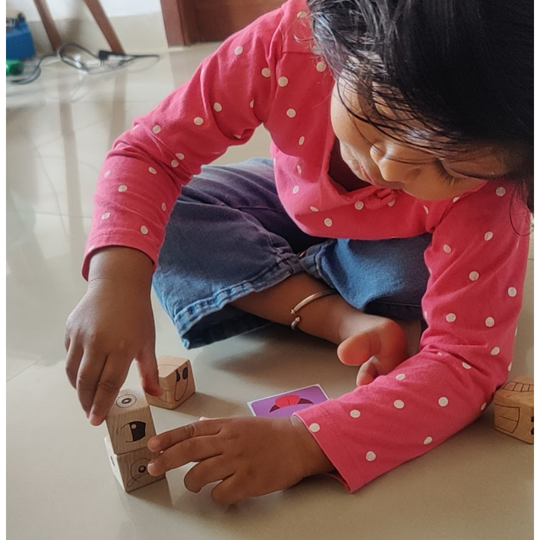 Child using wooden expression cubes and challenge cards during a hands-on matching cube game.