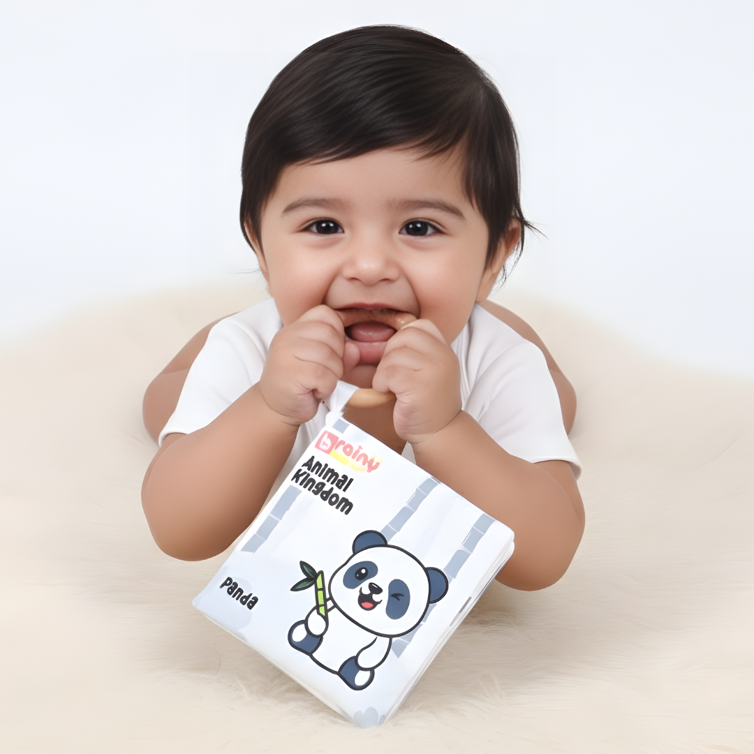 Baby exploring the BrainyTots Montessori High-Contrast Cloth Book – Early Seeing & Calm Play Book for Newborns 0–12 Months while chewing the attached natural Neem wood teether. The soft crinkle sensory book with bold jungle illustrations supports visual development, sensory exploration, teething relief, early language learning, and calm independent play.