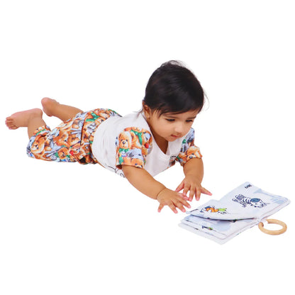 Baby reaching toward the BrainyTots Montessori High-Contrast Cloth Book during tummy time, encouraging reaching, visual tracking, hand-eye coordination, neck and core strength, and early sensory exploration through high-contrast animal illustrations.