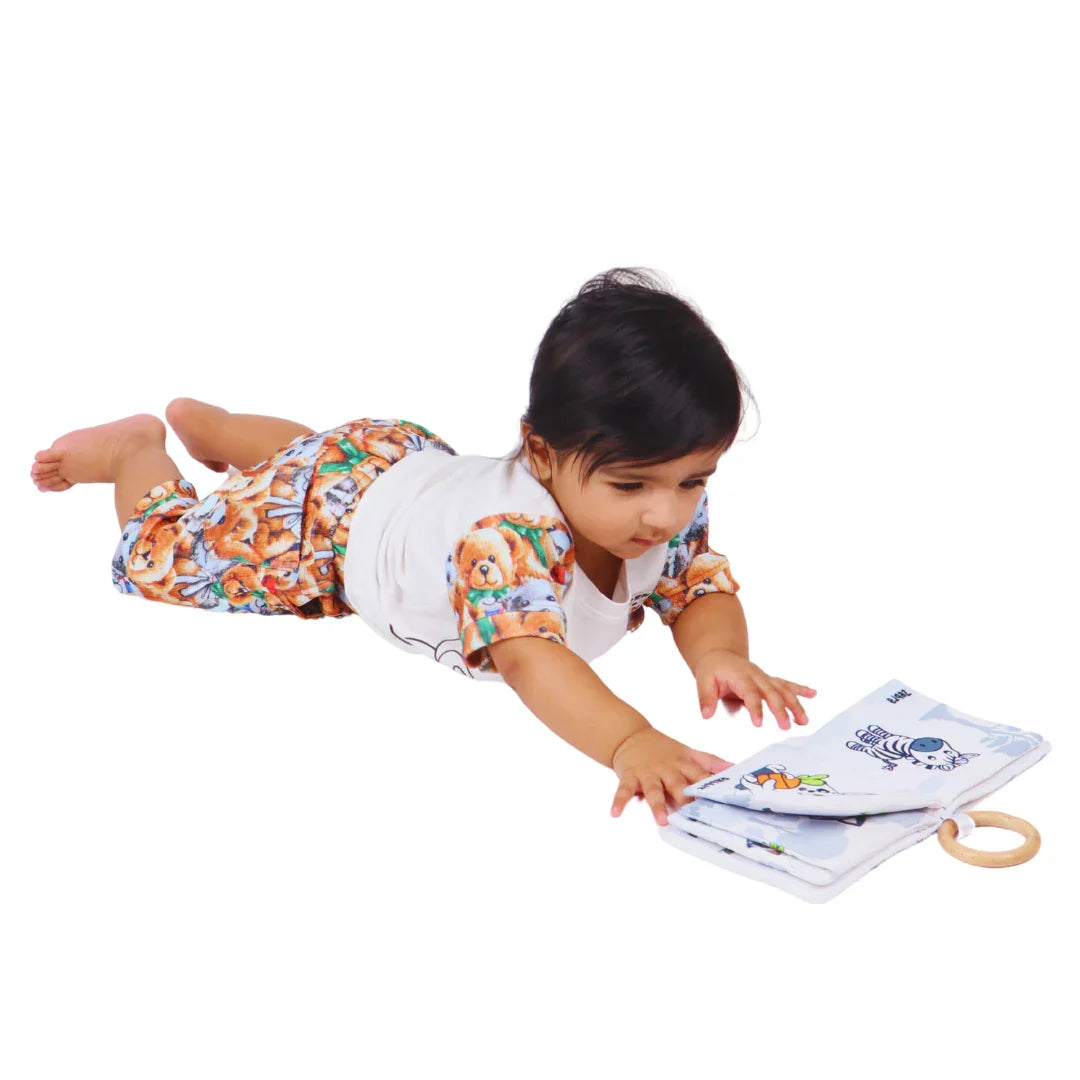 Baby reaching for the BrainyTots Montessori High-Contrast Cloth Book during tummy time, encouraging visual tracking, reaching, hand-eye coordination, sensory exploration, neck strength, and early cognitive development through high-contrast animal illustrations.