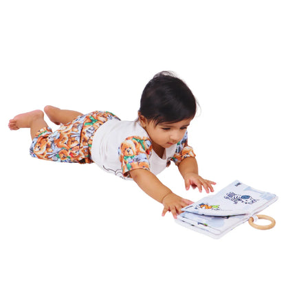 Baby reaching for the BrainyTots Montessori High-Contrast Cloth Book during tummy time, encouraging visual tracking, reaching, hand-eye coordination, sensory exploration, neck strength, and early cognitive development through high-contrast animal illustrations.
