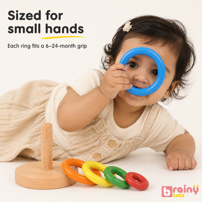 Baby holding the large blue ring from the BrainyTots Wooden Ring Stacker, demonstrating easy-to-grip colorful rings designed for babies aged 6–24 months. This Montessori-inspired wooden toy supports fine motor skills, hand-eye coordination, grasp development, color recognition, and independent learning through hands-on play.