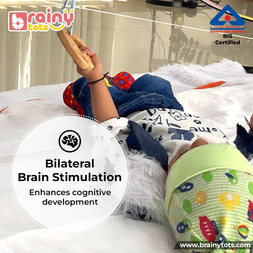 Baby playing with the BrainyTots Neem Wood Teether hanging from a Montessori play gym, supporting bilateral hand coordination, fine motor development, grasping skills, sensory exploration, and independent play during tummy time.