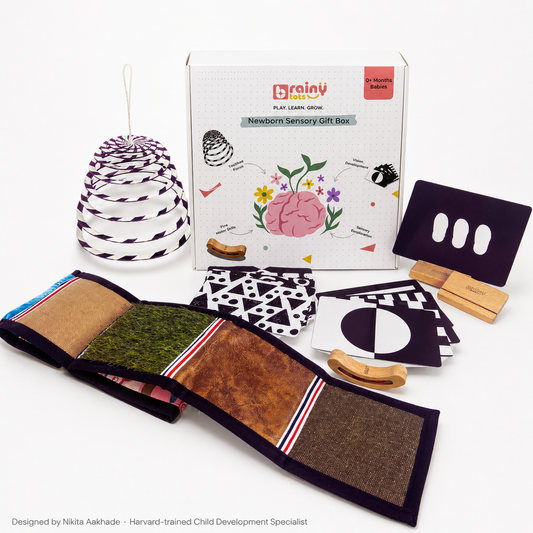BrainyTots Newborn Sensory Gift Box, a 6-in-1 baby development kit for 0–6 months featuring high-contrast flashcards, sensory texture mat, spiral hanging mobile, busy beads rattle, and flashcard stands for visual, sensory, and motor development.