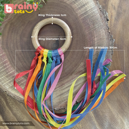 BrainyTots Rainbow Ribbon Wooden Teether size guide showing a natural Neem wood teether ring with a 6 cm diameter, 1 cm ring thickness, and seven colorful 30 cm satin ribbons designed to soothe sore gums, encourage grasping, and support sensory and fine motor development for babies aged 2 months and above.