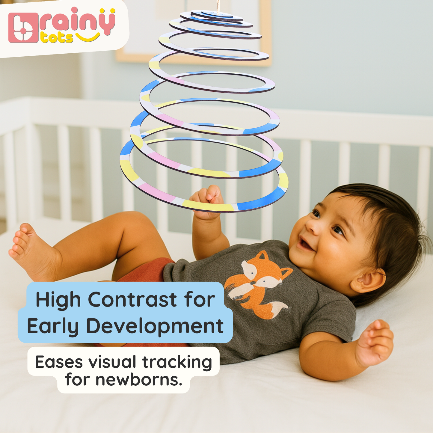 Newborn baby smiling and visually tracking the BrainyTots Spiral Hanging Mobile above the crib. This Montessori-inspired natural wooden mobile encourages early visual tracking, focus, concentration, and healthy visual development with high-contrast spiral patterns for babies aged 0–3 months.