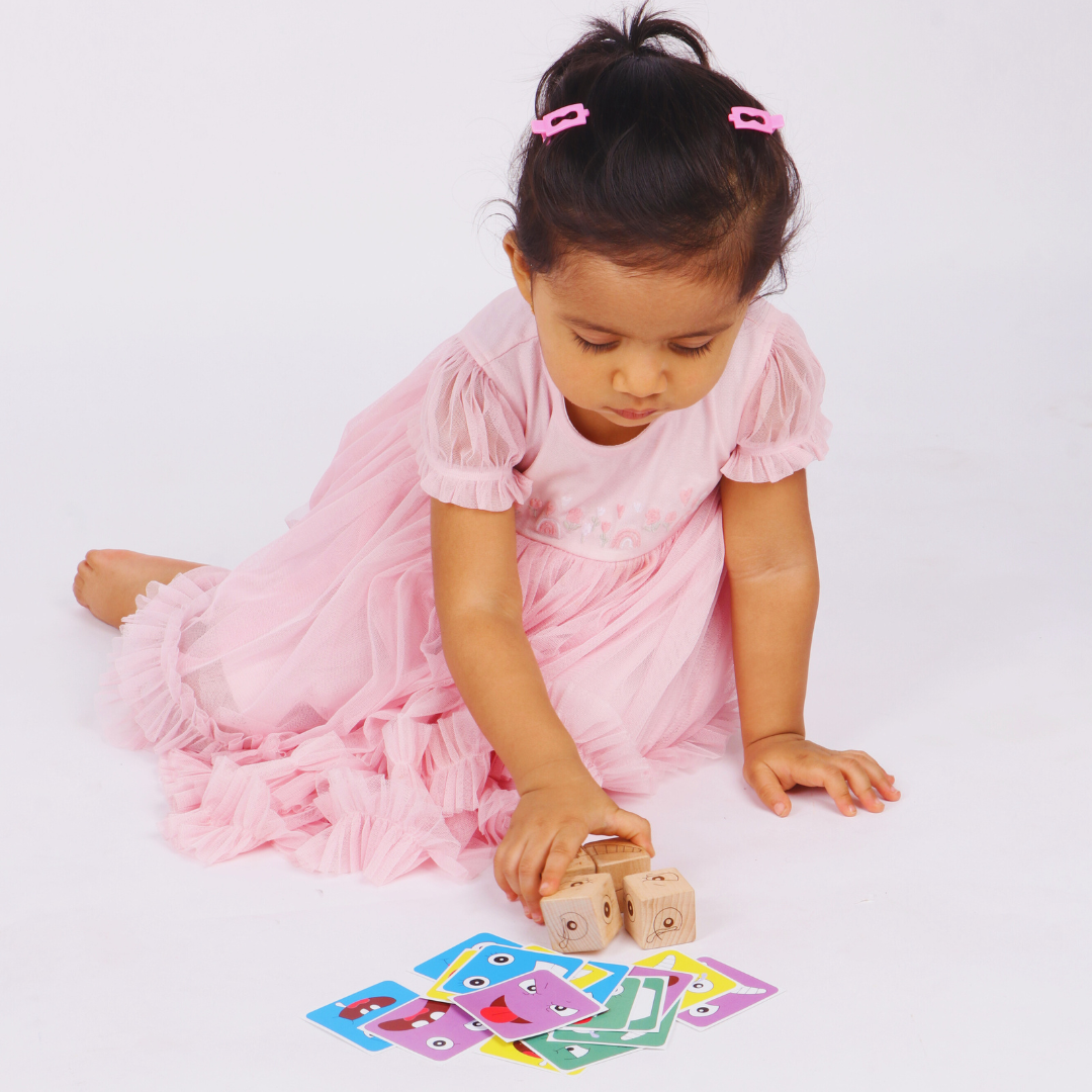 Child holding a wooden expression cube while playing with Face Match Fun challenge cards.