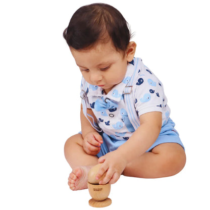 Baby sitting on a white background carefully placing a natural wooden egg into the cup piece of the Montessori puzzle, demonstrating balance, precision, and fine motor skill development for infants 6–15 months.