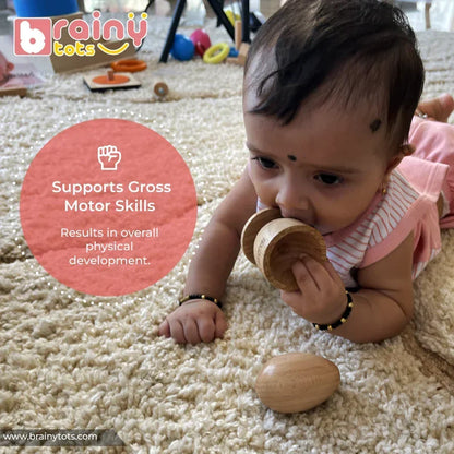 Baby on tummy during tummy time mouthing a natural wooden Montessori egg and cup puzzle cup piece, with the egg resting on a soft textured rug, supporting gross motor skills and overall physical development for infants 6–15 months.
