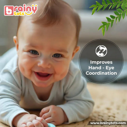 Smiling newborn baby during tummy time using the BrainyTots Montessori Neem Wood Teether Gift Set to develop hand-eye coordination, sensory skills, reaching ability, and early motor development.