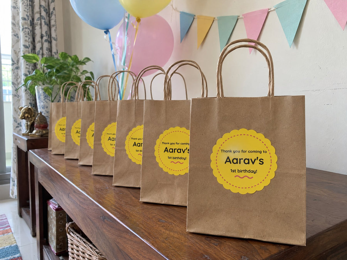 Kraft gift bags with yellow thank-you stickers on a party table